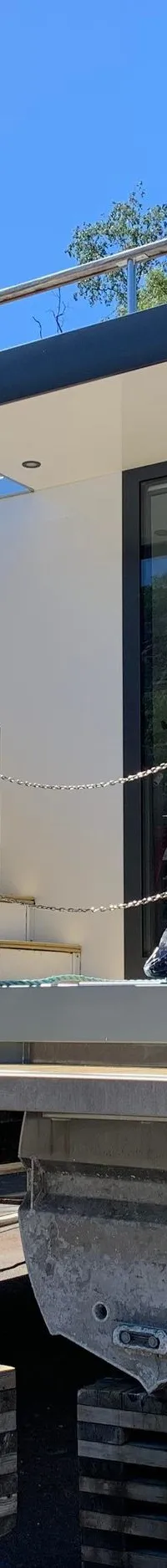 Een moderne woonboot met grijze en houtkleurige panelen staat op houten blokken op de wal, met grote ramen en een dakterras.