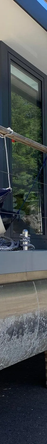 Een moderne woonboot staat op houten blokken op de wal, met een grijze romp, grote ramen en een reling.