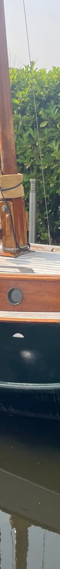Een donkergroene zeilboot met houten dek en kajuit ligt in het water naast een kleinere boot met een Yamaha buitenboordmotor.