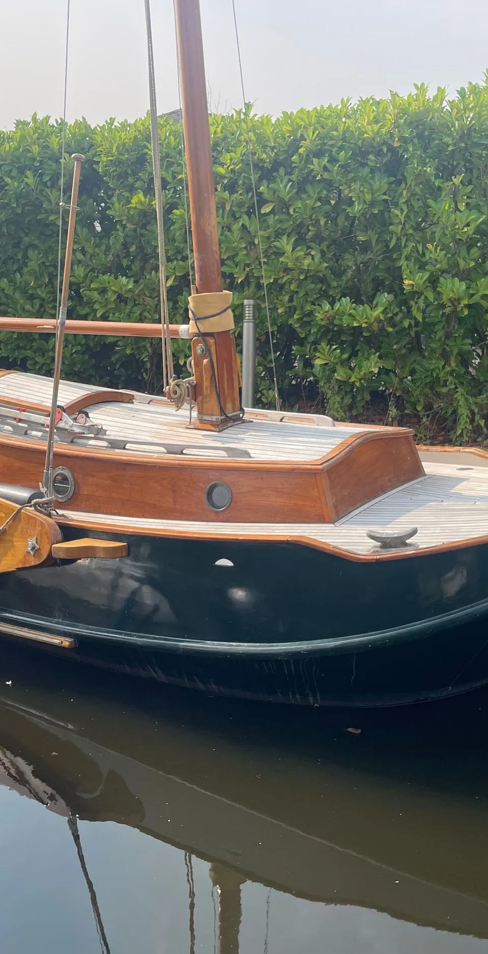 Een donkergroene zeilboot met houten dek en kajuit ligt in het water naast een kleinere boot met een Yamaha buitenboordmotor.