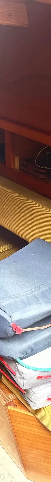 De foto toont het interieur van een boot met houten wanden, een tafel, banken met kussens en een kooktoestel.