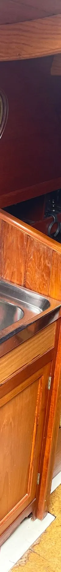 De foto toont een houten kajuit met een aanrecht, spoelbak, kastjes, een tafel met bloemen en een toilet. — Gipon Grundel 800