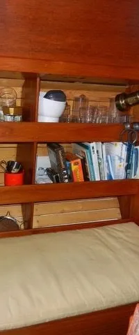 Een houten interieur met planken vol spullen, een bankje met kussen en een patrijspoort in het plafond.