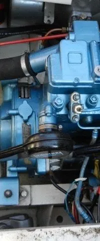 Een blauwe scheepsmotor met diverse slangen en bedrading is zichtbaar in een motorruimte.