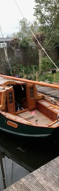 Een donkergroene zeilboot met houten dek en kajuit ligt aangemeerd aan een houten steiger. — Gipon Grundel 800