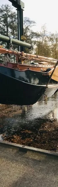 Een donkergroene zeilboot hangt aan een hijskraan boven een wateroppervlak met bladeren. — Gipon Grundel 800
