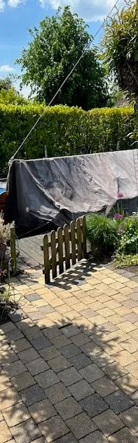 Een boot afgedekt met een donker zeil staat in een tuin met bestrating, gras en bomen. — Gipon Grundel 800