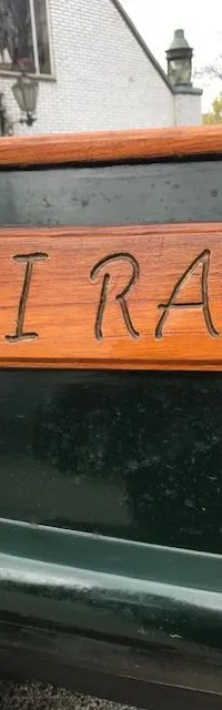 Een houten naambord met de ingegraveerde tekst "SAI RAM" is bevestigd op een donkergroene romp van een boot.