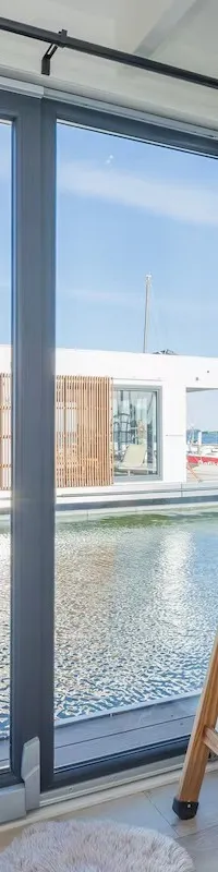 Een kamer met een stapelbed en een glazen schuifdeur die uitkijkt op water en een drijvend gebouw.
