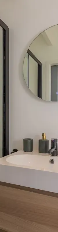 Een badkamer met een douchecabine, een wastafel met houten onderkast, een ronde spiegel en een stopcontact.