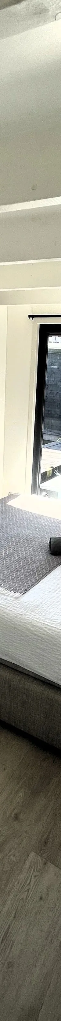 Een slaapkamer met een tweepersoonsbed, houten vloer en twee glazen schuifdeuren die uitkijken op een jachthaven.