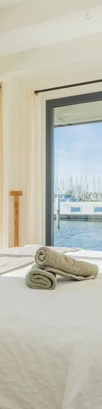 Een slaapkamer met een tweepersoonsbed en uitzicht op een haven vol zeilboten door grote ramen.