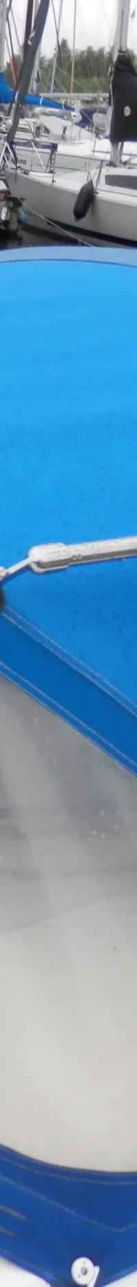 Een blauwe buiskap met doorzichtige ramen is zichtbaar op een witte zeilboot, met andere boten in de achtergrond.