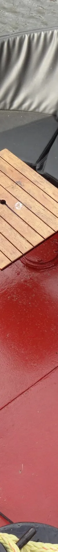 Een bovenaanzicht van de kuip van een boot met rode vloer, zwarte kussens en een houten tafelblad. — Garnalenkotter 15.50