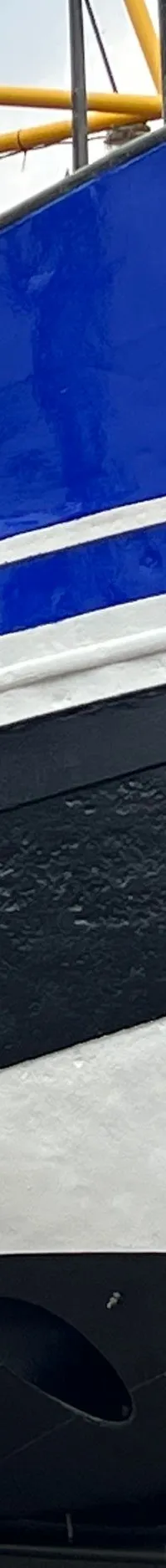 Een blauw-zwart-witte boot met "WR53" op de boeg staat op de wal, met een persoon op een ladder ernaast.