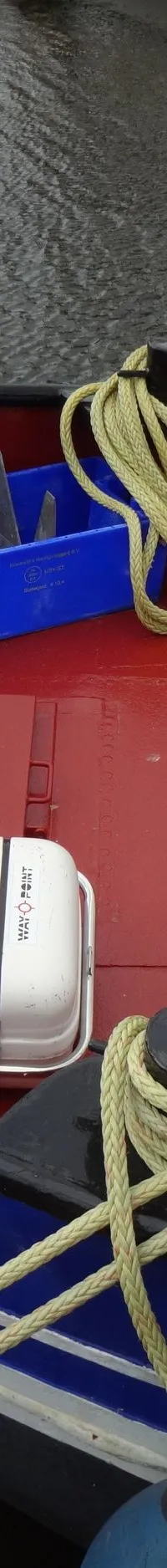 Een rood dek van een boot met blauwe en witte accenten, touwen, een reddingsvlot en diverse bakken. — Garnalenkotter 15.50