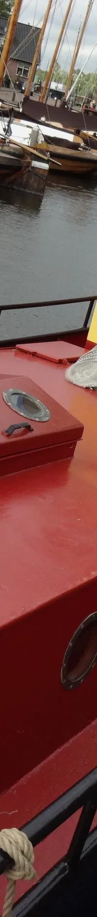 Een rode boot met gele opbouw en blauw dak ligt aangemeerd in een haven met andere boten. — Garnalenkotter 15.50
