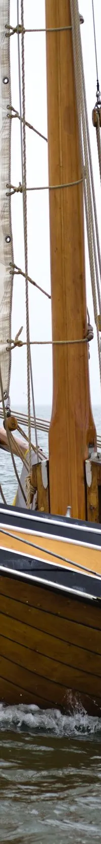 Een houten zeilboot met twee personen aan boord vaart op water onder een grijze lucht. — Boeier Lantinga 900