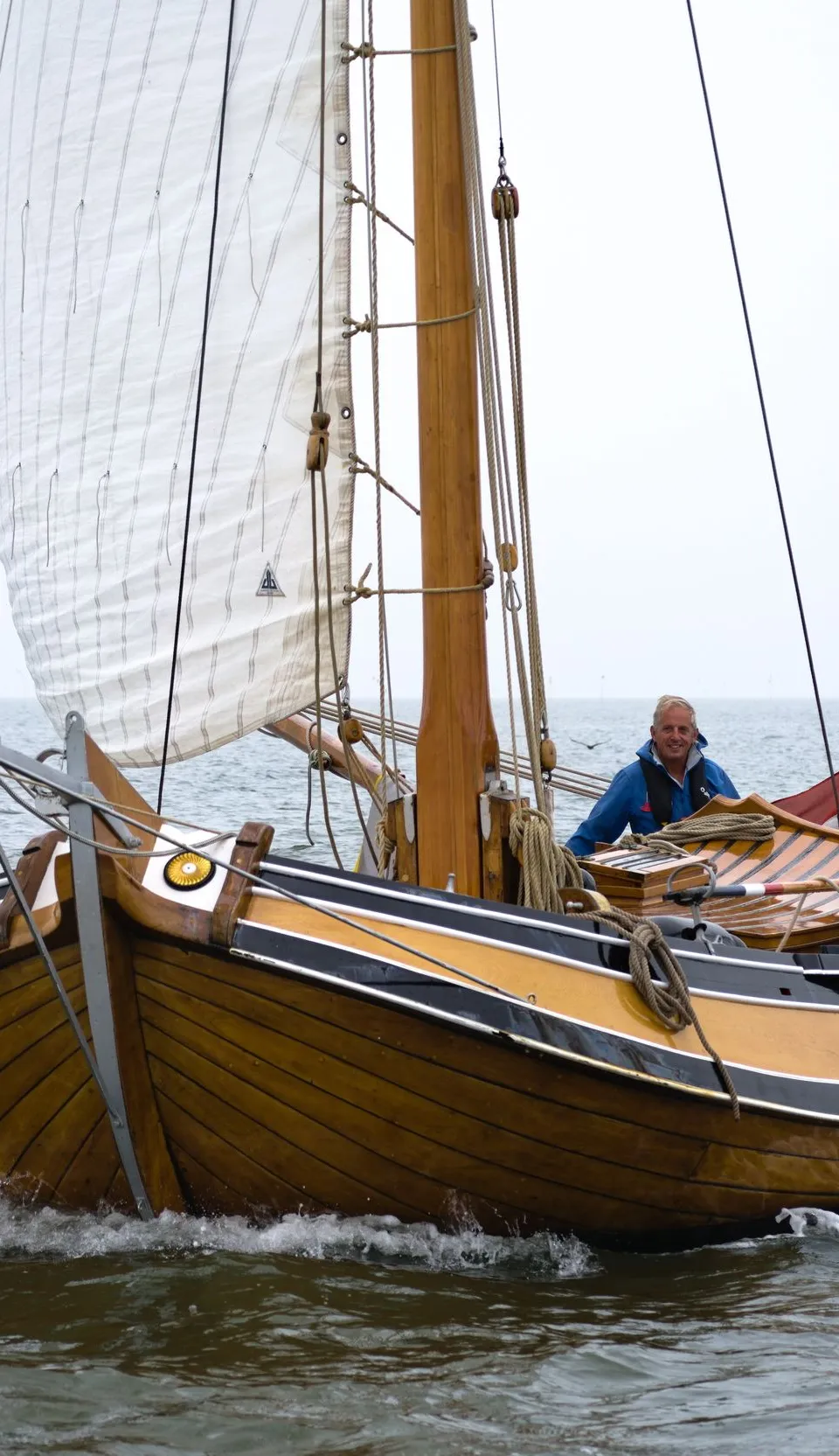 Een houten zeilboot met twee personen aan boord vaart op water onder een grijze lucht. — Boeier Lantinga 900