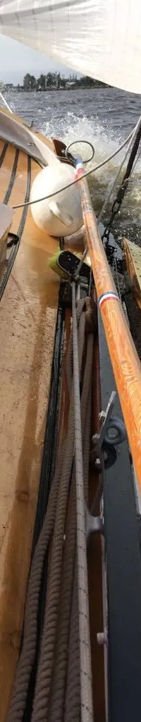 Een houten zeilboot vaart door woelig water, met een wit zeil en een stootwil zichtbaar. — Boeier Lantinga 900