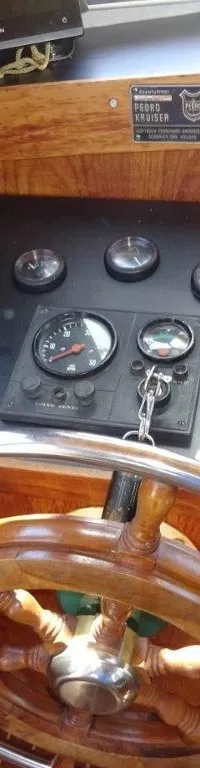 Een houten stuurwiel met metalen spaken en een zwart dashboard met diverse meters en schakelaars.