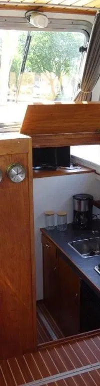 De foto toont het interieur van een boot met een houten stuurwiel, een kombuis en een slaapbank. — Pedro Kruiser 1000 AK