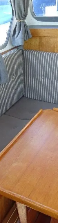 Een interieur van een boot met houten wanden, een hoekbank met gestreepte kussens en een houten tafel.