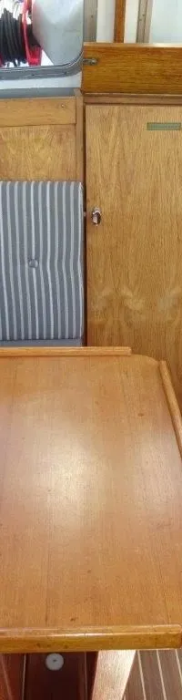 De foto toont het interieur van een boot met houten wanden, een houten tafel, gestreepte kussens en een houten vloer.