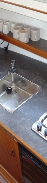 Een kombuis met een gootsteen, koffiezetapparaat, waterkoker op een gasfornuis en diverse glazen en mokken.