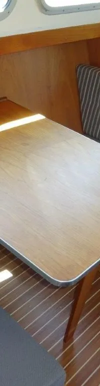 Een houten kajuitinterieur met een tafel, twee zitbanken met kussens en een houten vloer.