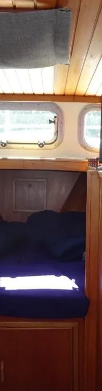 De foto toont het interieur van een boot met een houten plafond, banken, een tafel, een bed, een televisie en een…