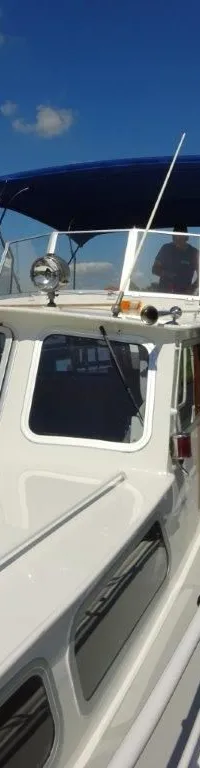 Een witte boot met blauwe kap ligt afgemeerd aan een houten steiger onder een blauwe lucht. — Pedro Kruiser 1000 AK