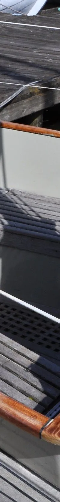 Een deel van het achterdek en de kuip van een zeilboot met houten banken, een lier en een zwart afdekzeil is zichtbaar.