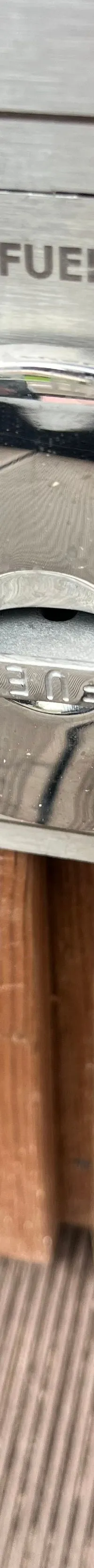 Een close-up van een zilverkleurige brandstofdop met het woord "FUEL" erop, gemonteerd op een houten oppervlak.