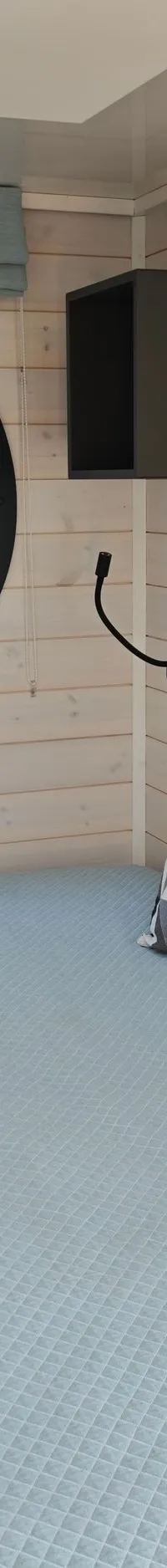 Een kajuit met een bed met lichtblauwe sprei, twee kussens, een rond patrijspoort, en houten wanden.