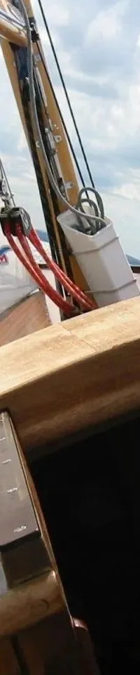 Een zeilboot vaart op water met een wit zeil, touwen en een houten dek onder een bewolkte hemel.