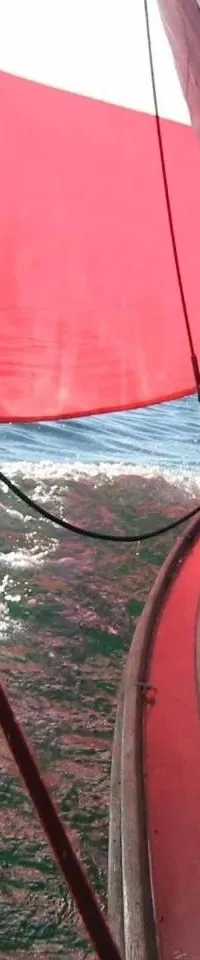 Een zeilboot met een rood zeil en een wit zeil vaart over water met zonlichtreflecties. — Begré Nordische Folkeboot 7.64
