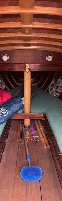 De foto toont het interieur van een houten boot met twee groene matrassen, een blauwe borstel en diverse spullen.