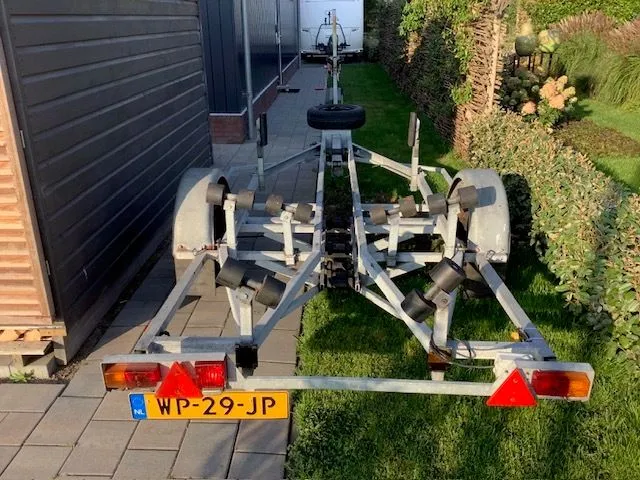 Een boot trailer met kenteken WP-29-JP staat op een oprit naast een heg en een schuur. — Randmeer Advance.