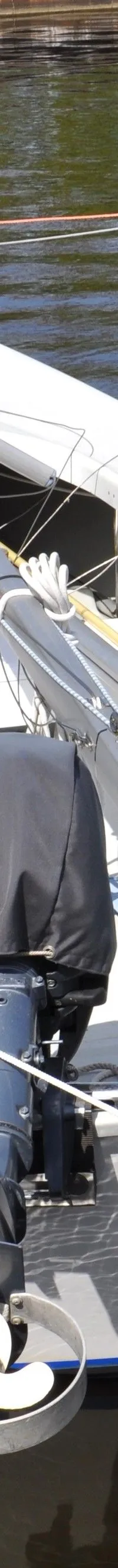 Een witte zeilboot met een blauwe streep en een buitenboordmotor met propellerbescherming ligt afgemeerd aan een houten…