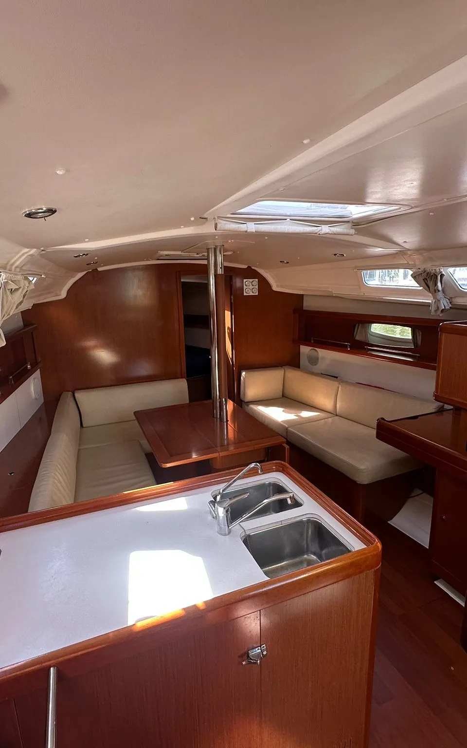 De foto toont het interieur van een boot met een kombuis, zithoek, houten meubels en ramen. — Beneteau Oceanis 37