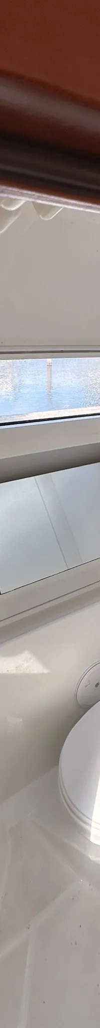 De foto toont een badkamer met een toilet, wastafel, spiegelkast en een raam met uitzicht op water.