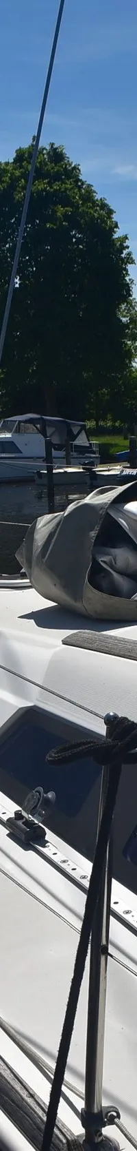 Een witte zeilboot ligt afgemeerd naast een houten woonboot, met een opgerold zeil op het dek. — Beneteau Oceanis 37