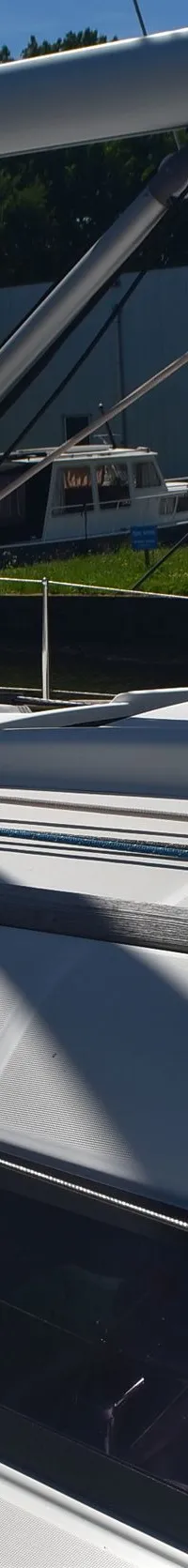 Een witte zeilboot met een grijze buiskap en een opgerolde grijze hoes voor het grootzeil, liggend aan een kade.