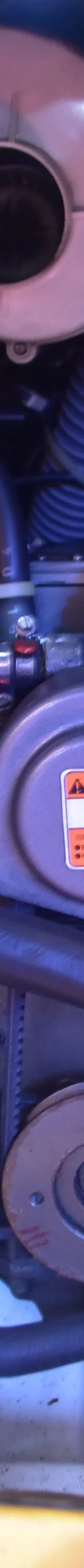 Een detailfoto van een scheepsmotor met diverse slangen, kabels en een waarschuwingssticker.