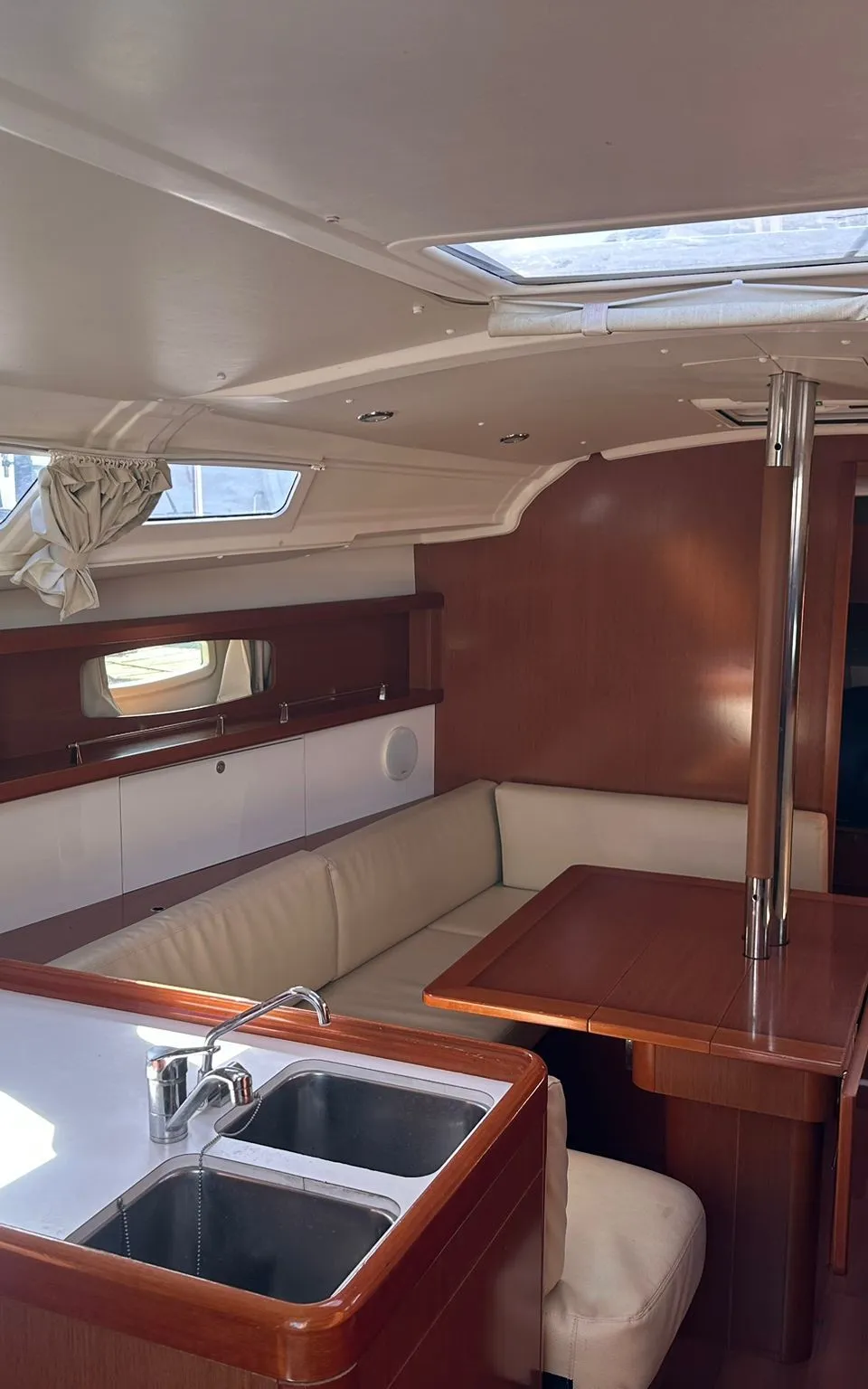 De foto toont het interieur van een boot met een kombuis, zithoek met tafel en een doorgang naar een hut.