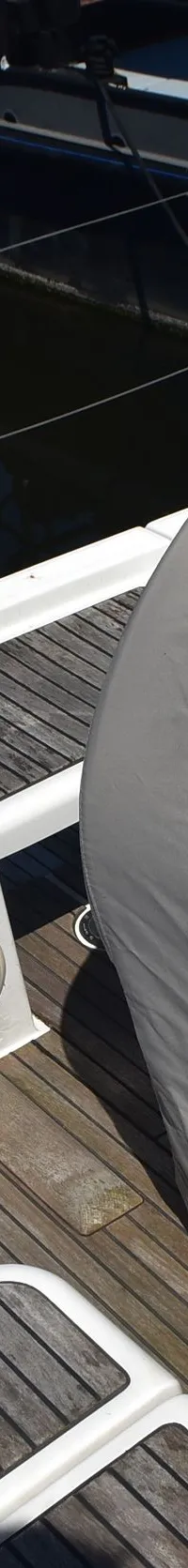 Een dek van een zeilboot met teakhouten planken, een grijze afdekhoes en een luidspreker. — Beneteau Oceanis 37