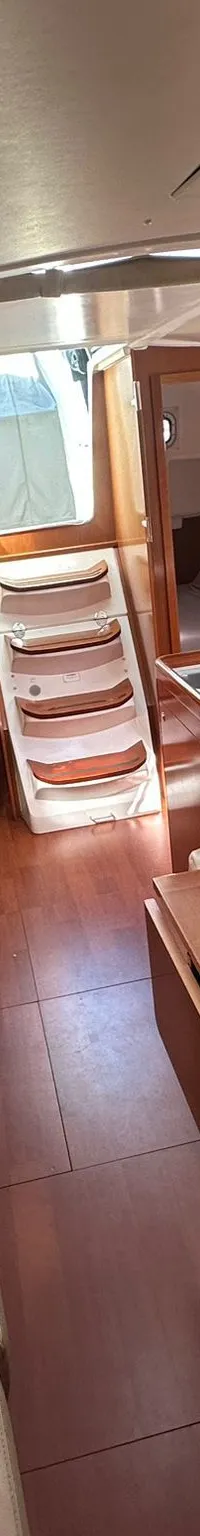 De foto toont het interieur van een boot met houten vloeren en meubels, lichte bekleding, een tafel en een kombuis.