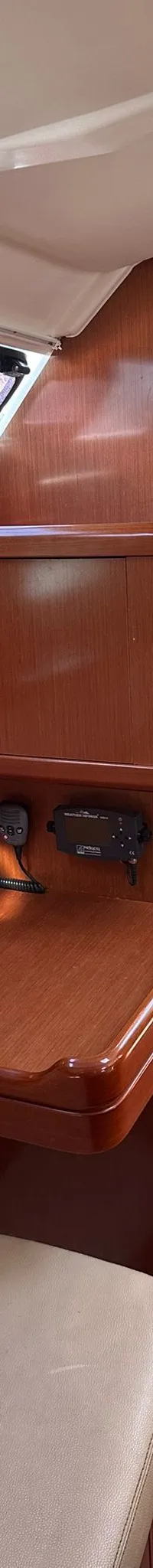 De foto toont het interieur van een boot met houten meubilair, een beige bank, ramen en een trap. — Beneteau Oceanis 37