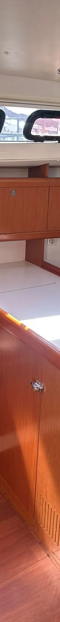 De foto toont een kombuis met een fornuis, oven, dubbele spoelbak en houten kasten, met een bank en ramen op de achtergrond.